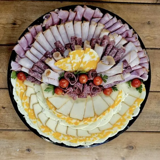 A deli platter of sliced ham, turkey, salami, cheddar and pepper jack with cherry tomatoes